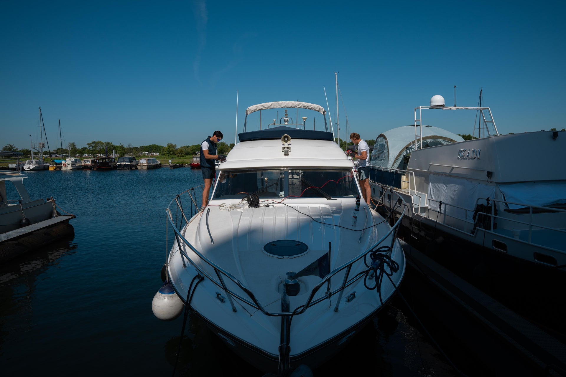 Twee YachtMates medewerkers voeren professioneel onderhoud uit aan een jacht in de haven.